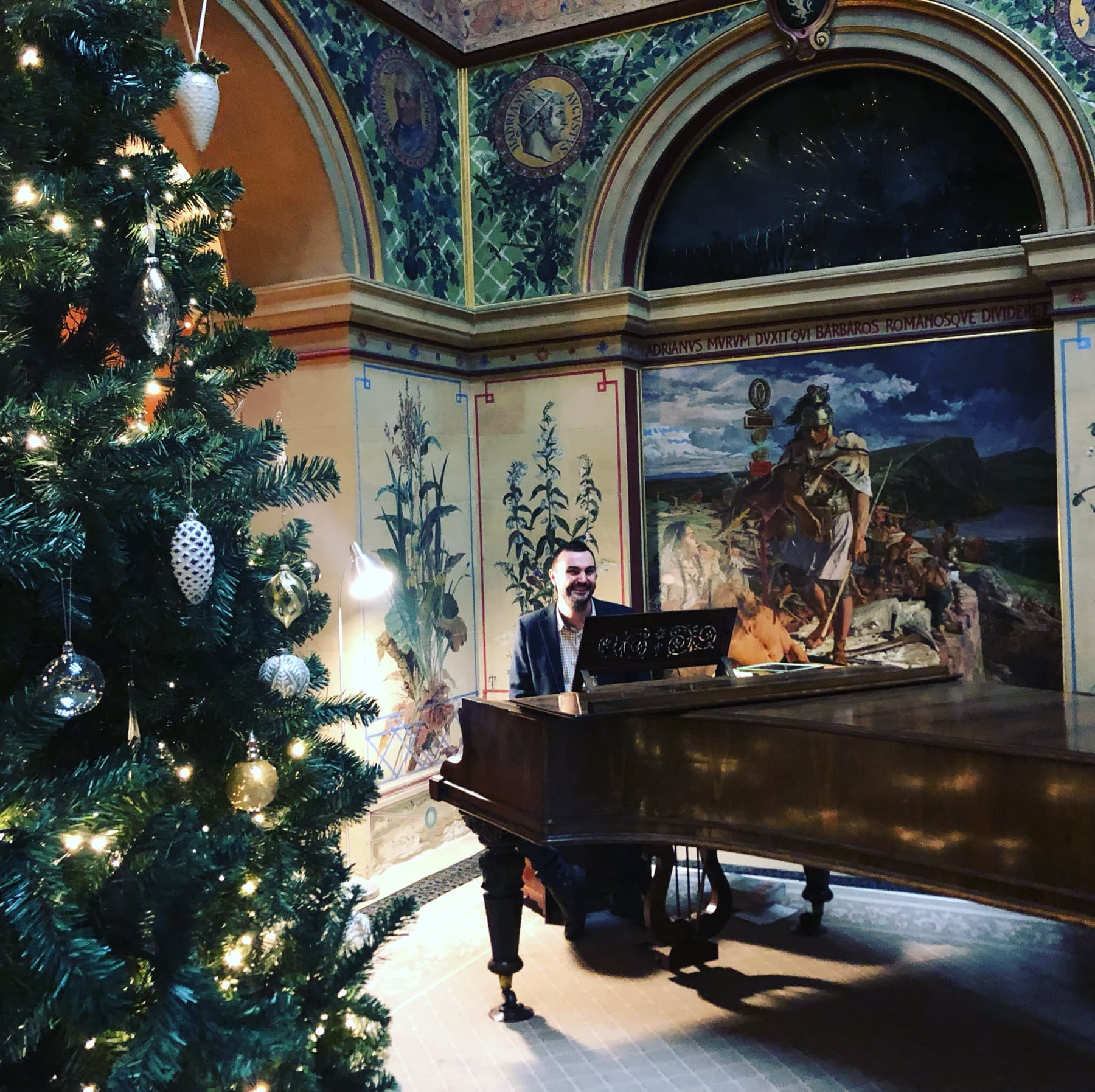 Phil Richardson playing a grand piano in an ornate hall beside a Christmas tree