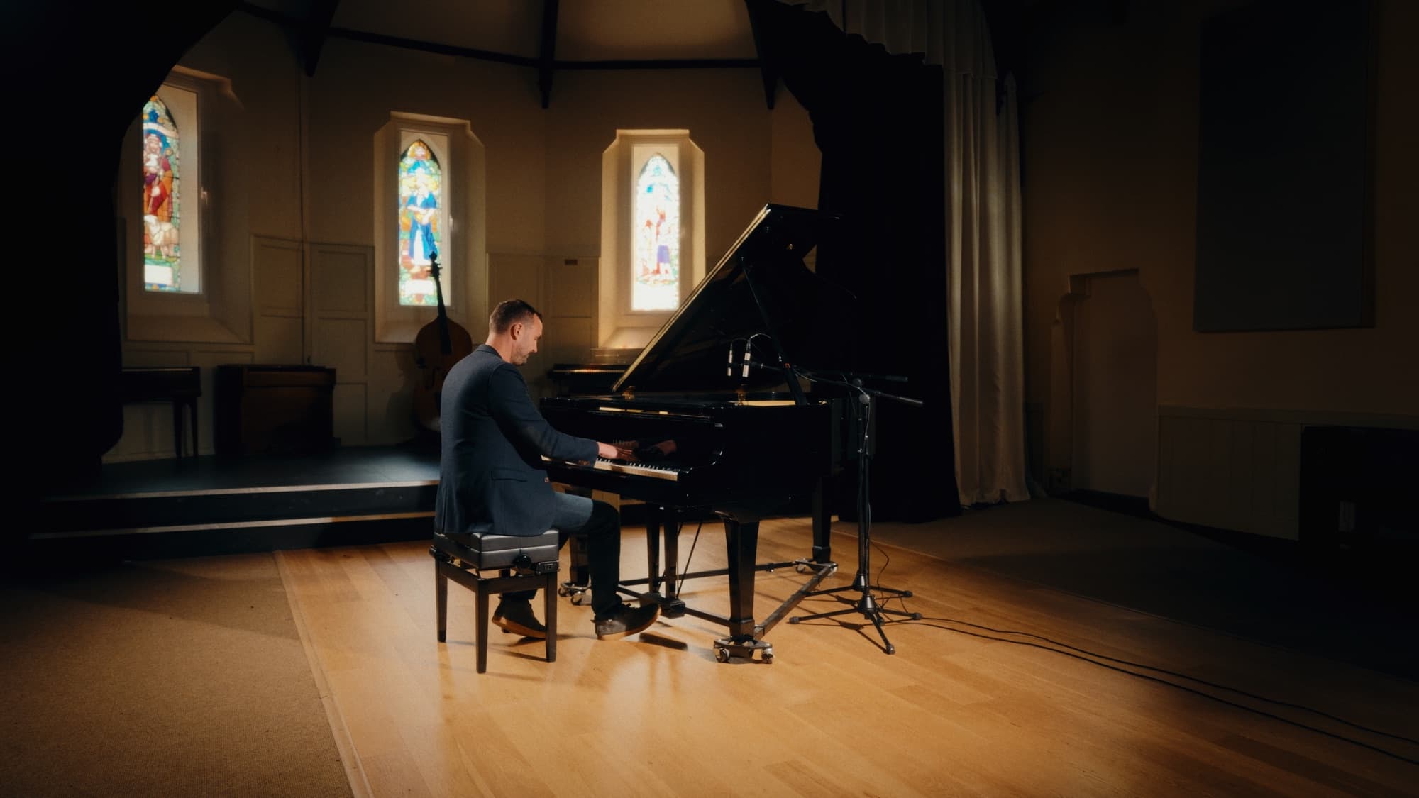 Phil Richardson playing a grand piano in a hall with stained glass windows